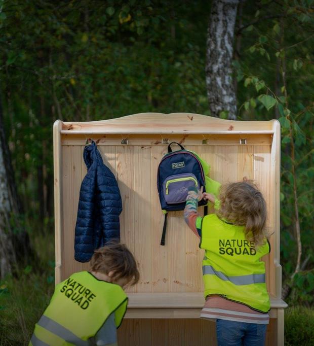 Due Panterini in gilet Nature Squad appendono zaini e giacche alla panca di legno nel bosco